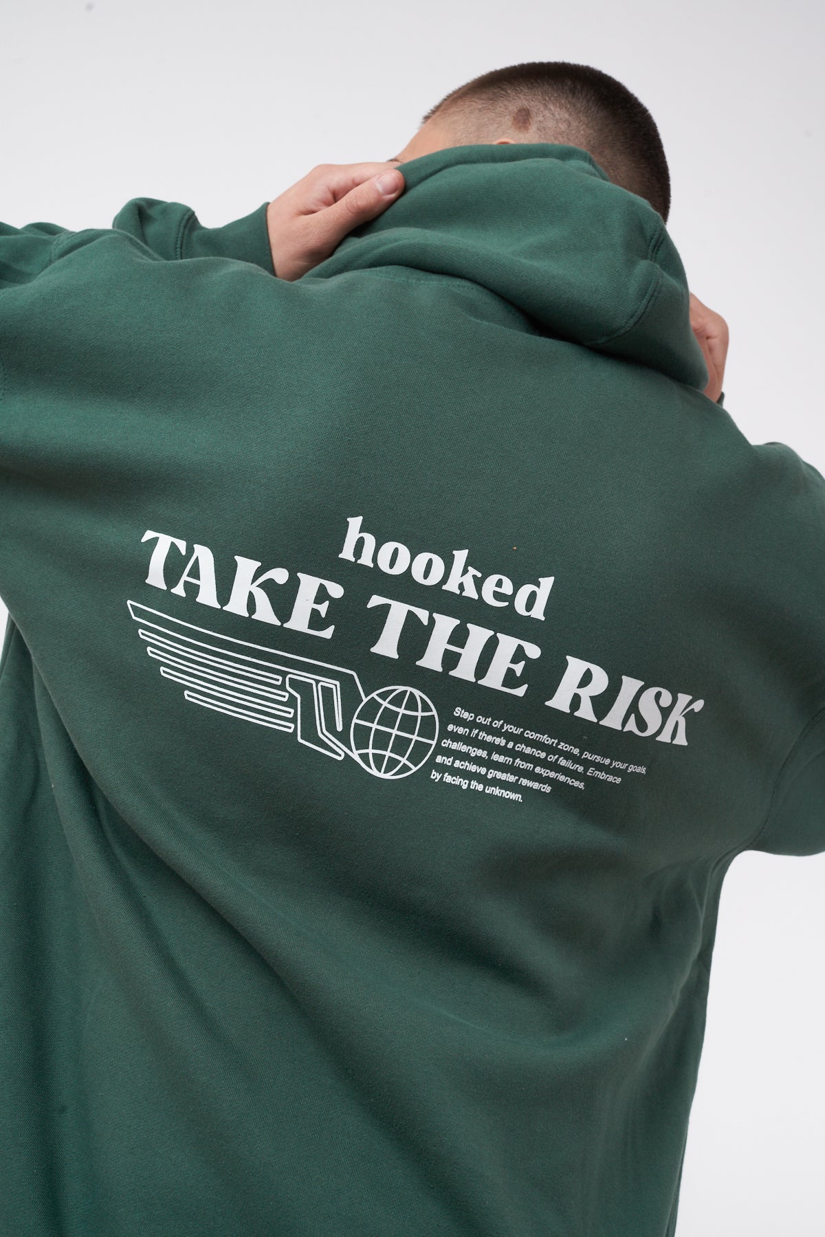 Green hoodie with 'hooked take the risk' text on the back, worn by a person.