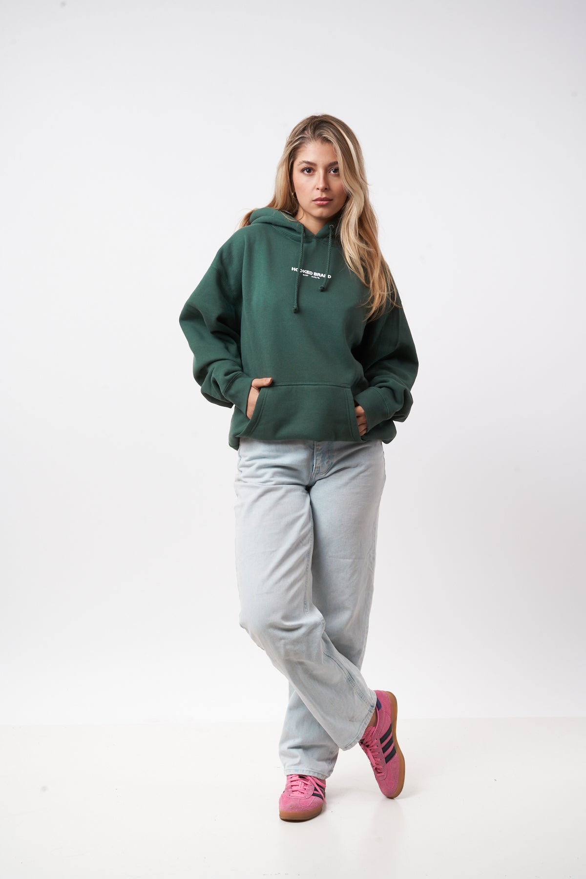 Woman wearing a green hoodie, gray sweatpants, and pink shoes on a white background