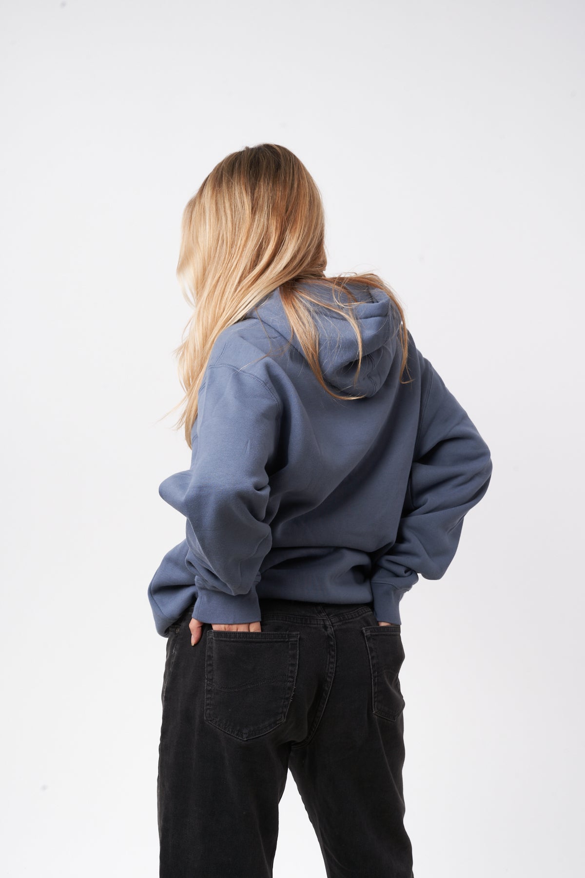 Person wearing a blue hoodie and black pants against a white background