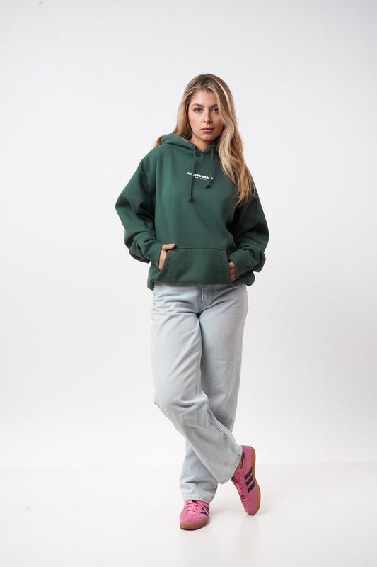 Woman wearing a green hoodie, gray sweatpants, and pink shoes on a white background